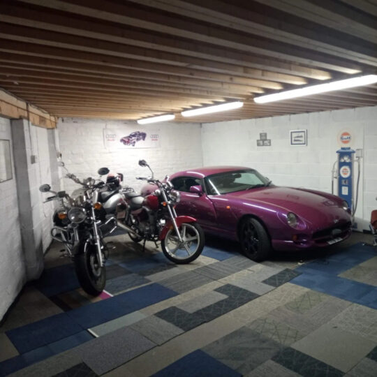 Garage with classic sports car, motorcycle and vintage petrol pump on blue tiled flooring