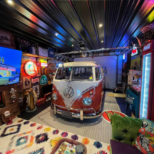 Classic red and white VW camper van in a colourful man cave with neon signs and vintage decor