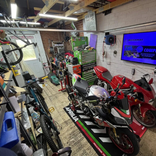 Motorcycle-filled man cave garage with Aprilia and other bikes alongside tools and signage