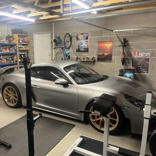 Grey Porsche parked in a well-organised car cave with wall-mounted memorabilia and artwork