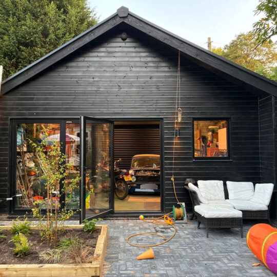 Black timber-clad garden building with open bifold doors revealing a workshop and seating area, set on Duramat flooring