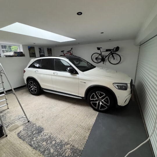 White Mercedes SUV parked in a residential garage with wall-mounted bicycles