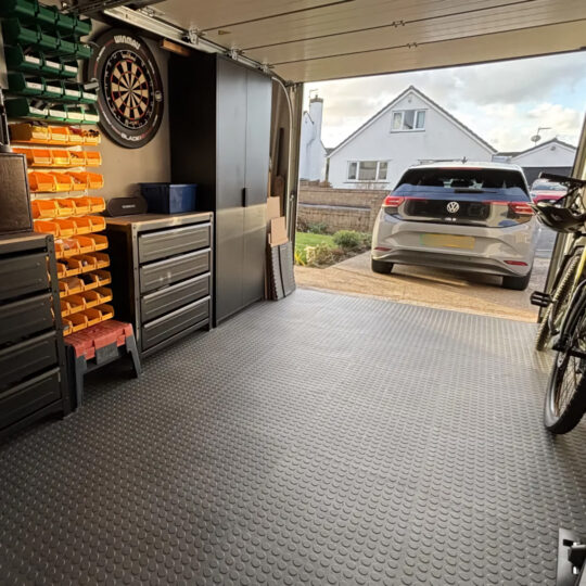 Tidy garage with Duramat flooring, dartboard on wall and open door showing driveway