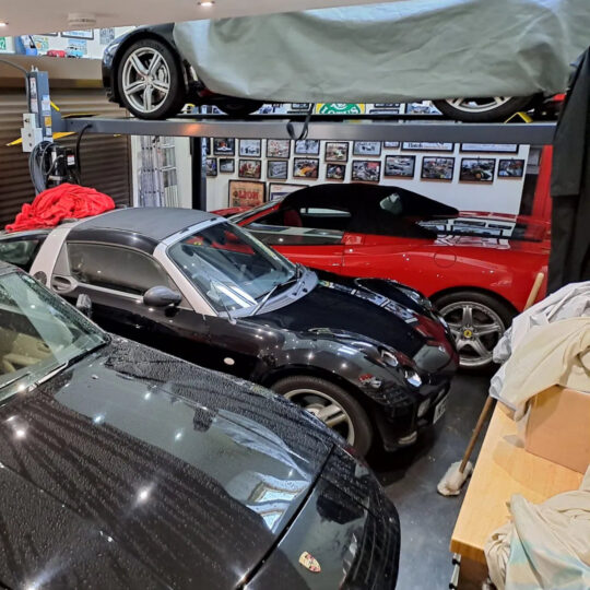Car cave garage with multiple vehicles stored on ground level and raised platform