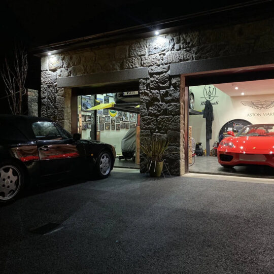 Illuminated car cave at night with Aston Martin signage and red sports car visible inside
