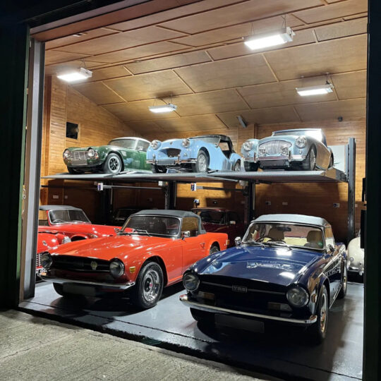 Classic car collection stored on two levels in a garage with cars on a raised mezzanine platform