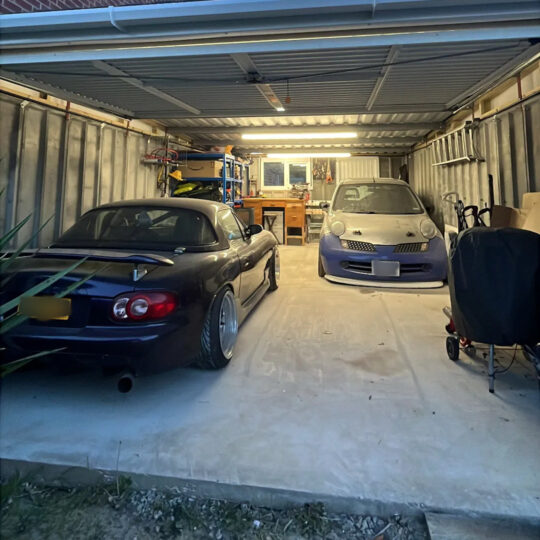 Multiple cars including a Mazda MX-5 stored in a metal-roofed garage barn