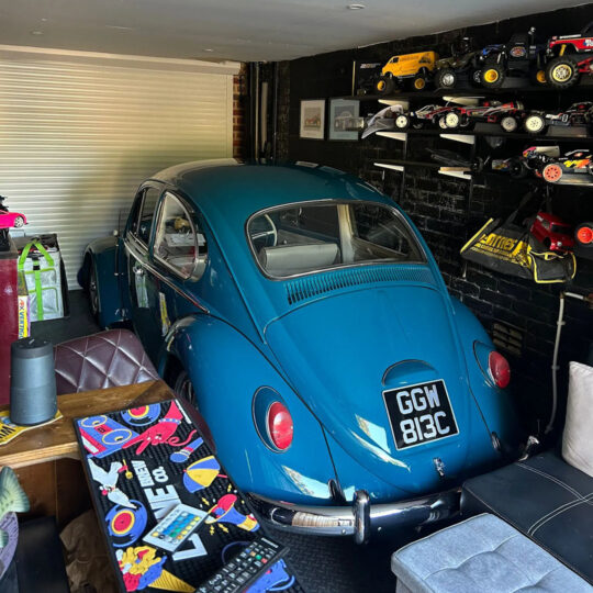 Blue classic Volkswagen Beetle in a garage surrounded by model car collection on shelves