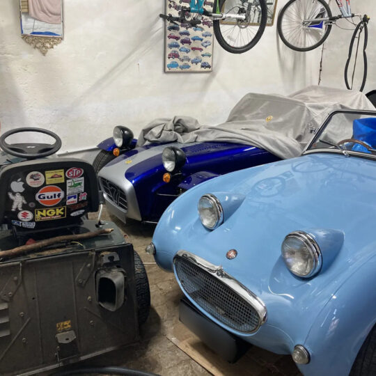 Blue classic Austin-Healey Sprite in a garage decorated with motorsport stickers and memorabilia