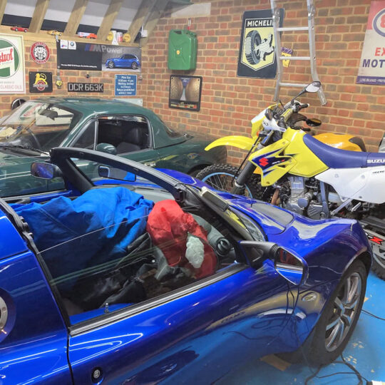 Blue sports car and motorcycles in a brick-walled garage with vintage Michelin signage