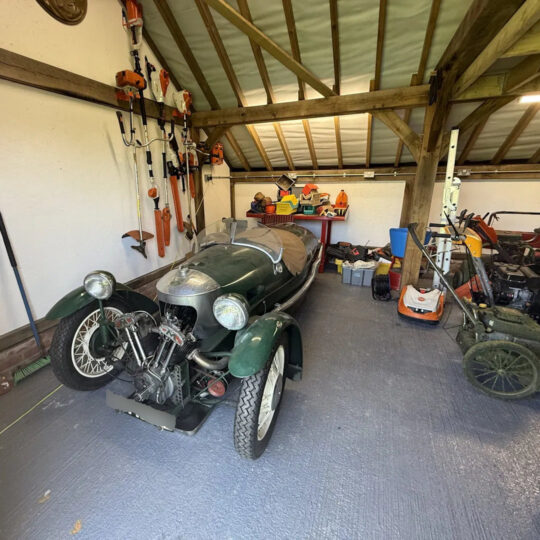 Vintage green three-wheeler Morgan car stored in a timber-framed barn garage