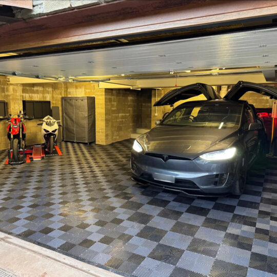 Tesla parked in a car cave with chequered Duramat flooring and motorcycle memorabilia