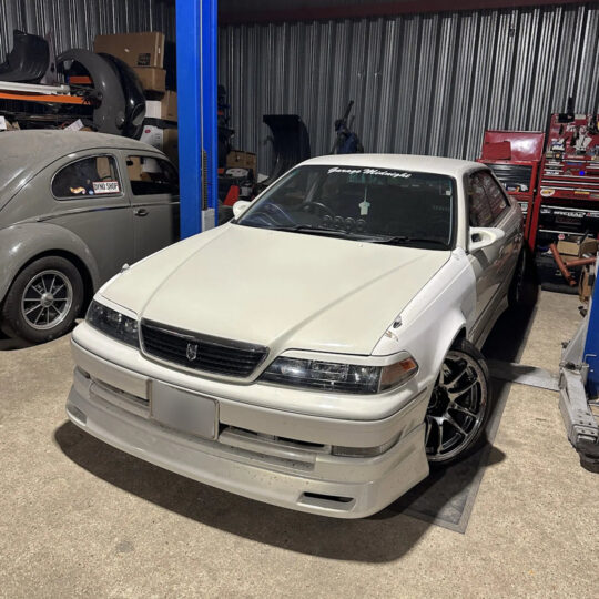 White modified Japanese saloon car parked inside a workshop garage