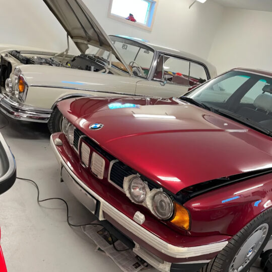 Red classic BMW alongside other vintage cars stored in a garage